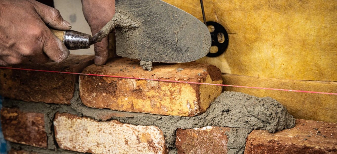 Hände, die Mörtel auf einen Ziegelstein auftragen, während eine Schnur gespannt ist.