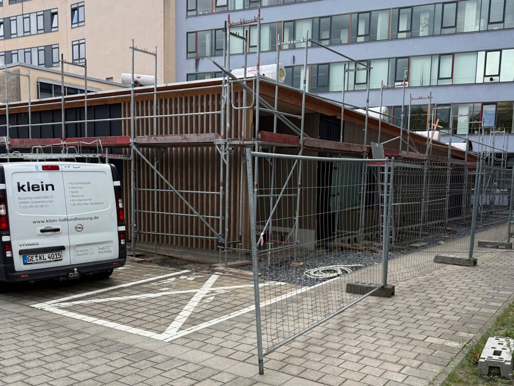 Baugerüst um ein Gebäude mit einem weißen Lieferwagen auf einem gepflasterten Parkplatz.