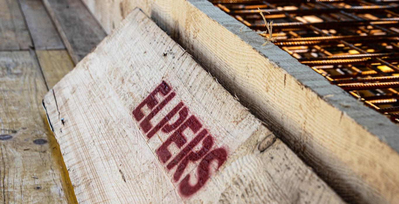 Holztafel mit dem Schriftzug "ELPERS" auf einer Baustelle.