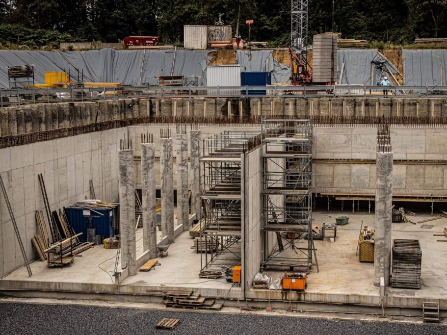 Baustelle mit Betonsäulen, Maschinen und Materialien in einer grubenartigen Struktur.