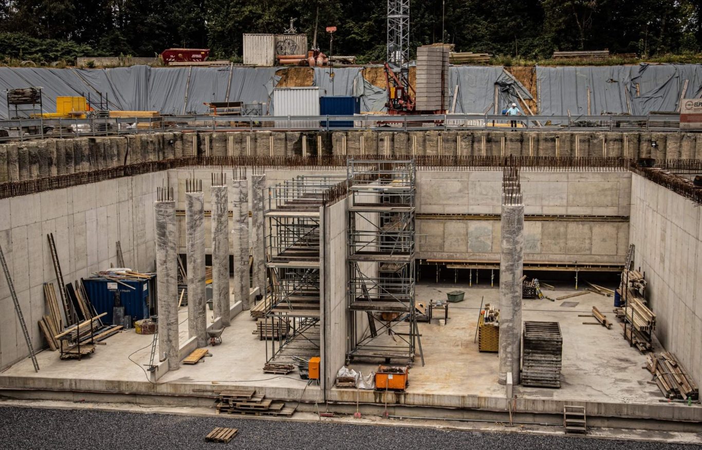 Baugrube mit Sicht auf Betonwände und Baugerüst, diverse Materialien liegen verstreut.