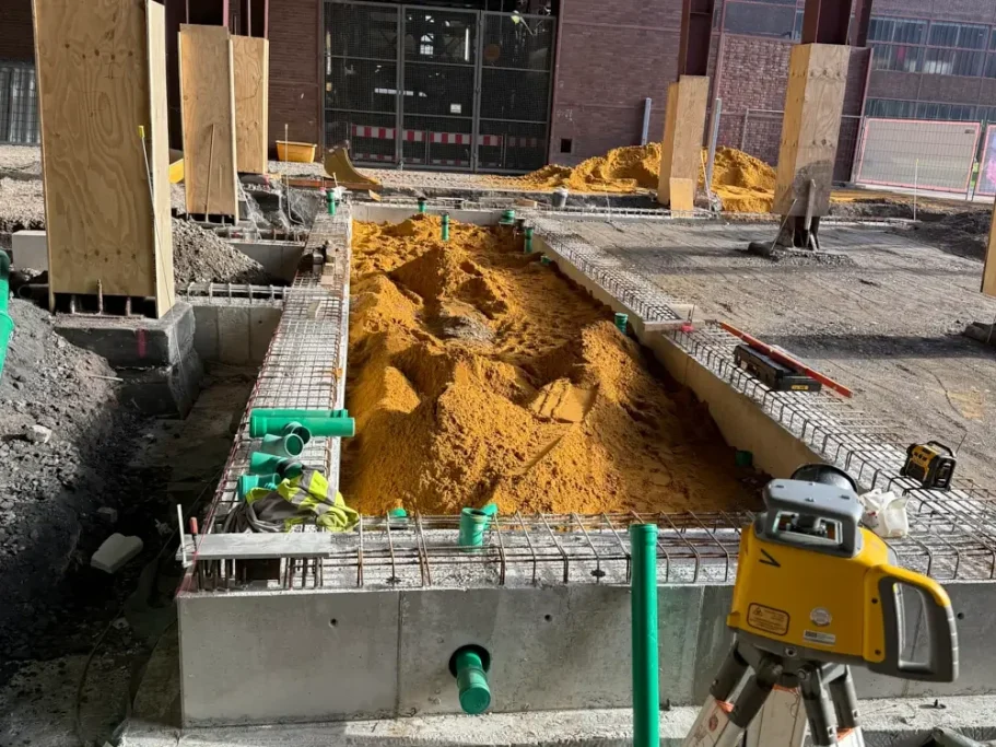 Bauarbeiten mit einem Sandbett und Baumaschinen auf einer Baustelle.