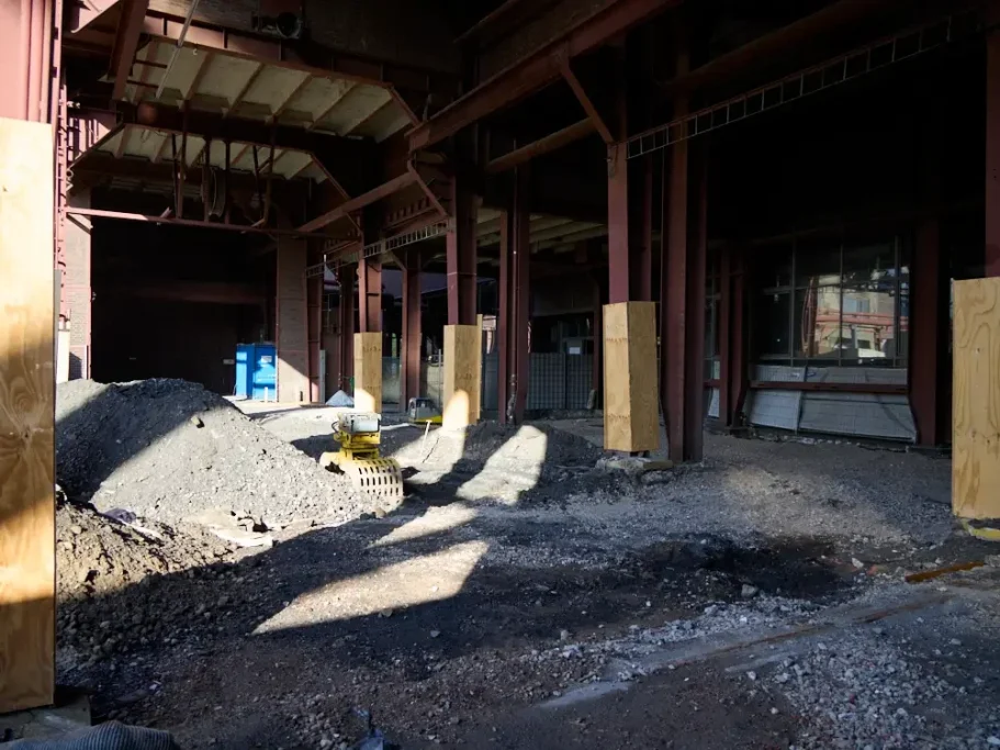 Baufeld mit Erdaushub und Holzverkleidungen in einem rohbauähnlichen Innenraum.