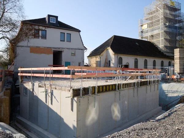 Bauplatz mit einem Erdgeschoss und ansässigen Gebäuden im Hintergrund.