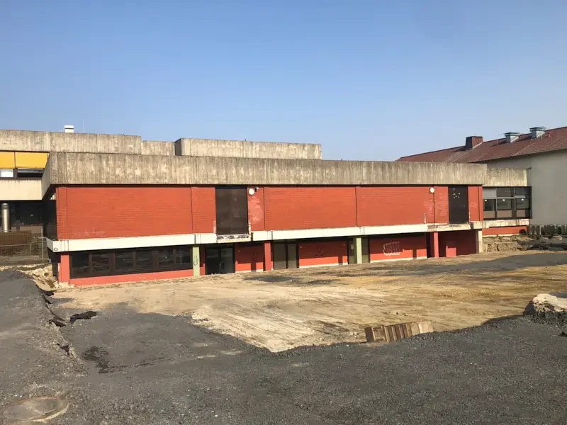 Roter Gebäudekomplex mit Betonakzenten, umgeben von unbefestigtem Gelände.