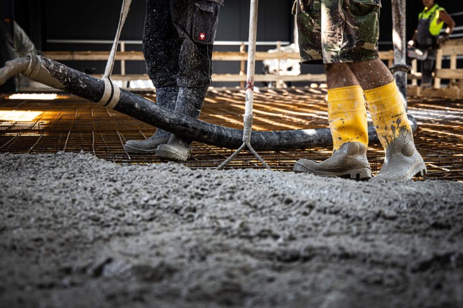 Arbeiter gießen Beton auf einer Baustelle, mit Gummistiefeln und einem Schlauch.