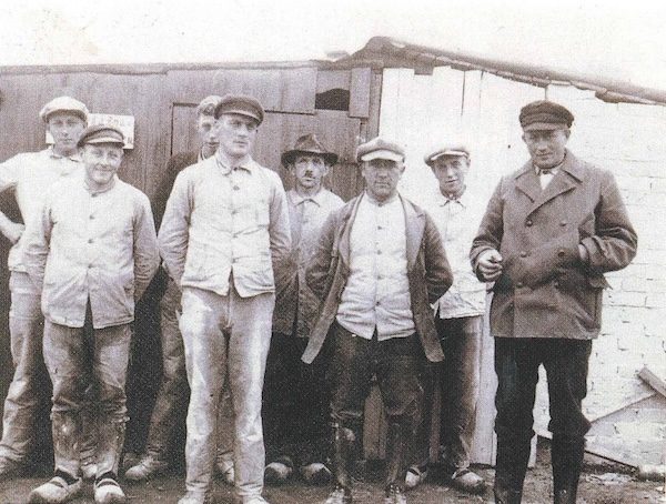Historische Gruppenaufnahme von sieben Männern in Arbeitskleidung.