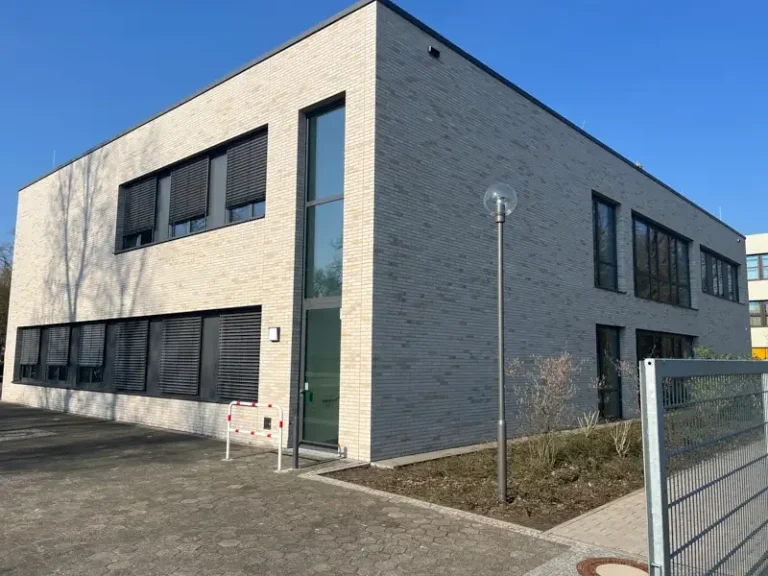 Moderne zweigeschossige Gebäude mit hellem Mauerwerk und großen Fenstern.