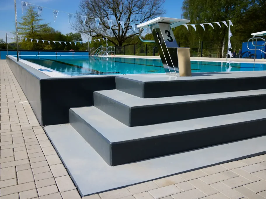 Drei graue Stufen führen zu einem Schwimmbecken mit blauem Wasser und Schwimmbahnen.
