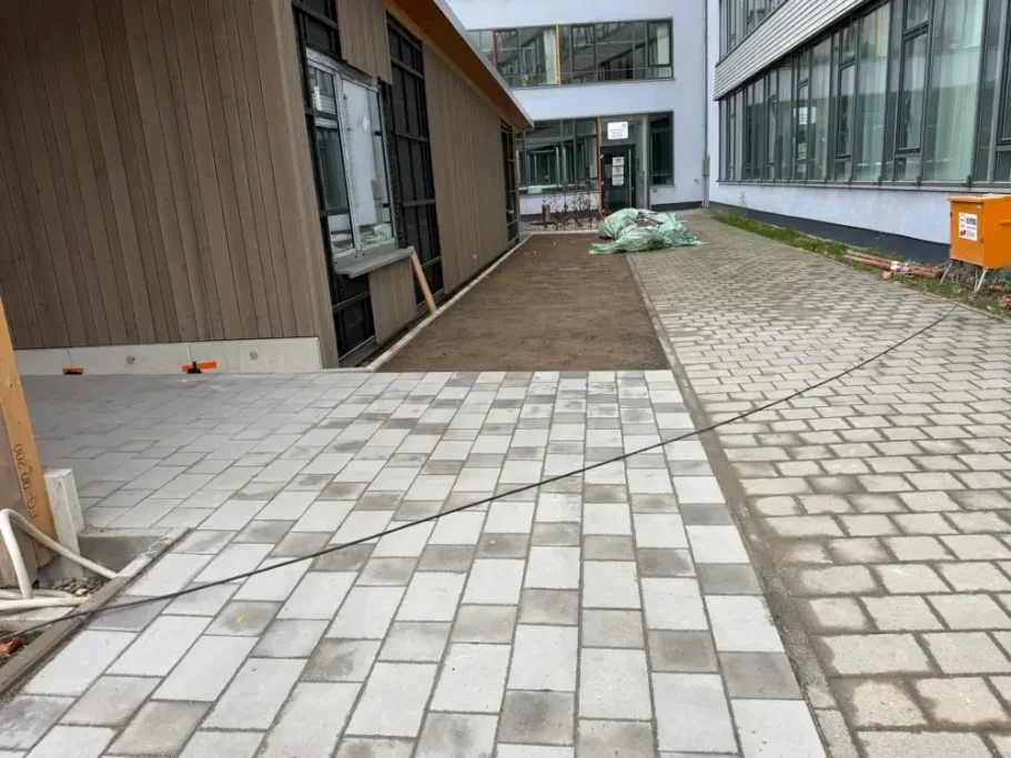 Neuer gepflasterter Gehweg zwischen Gebäuden und unbebautem Gelände.