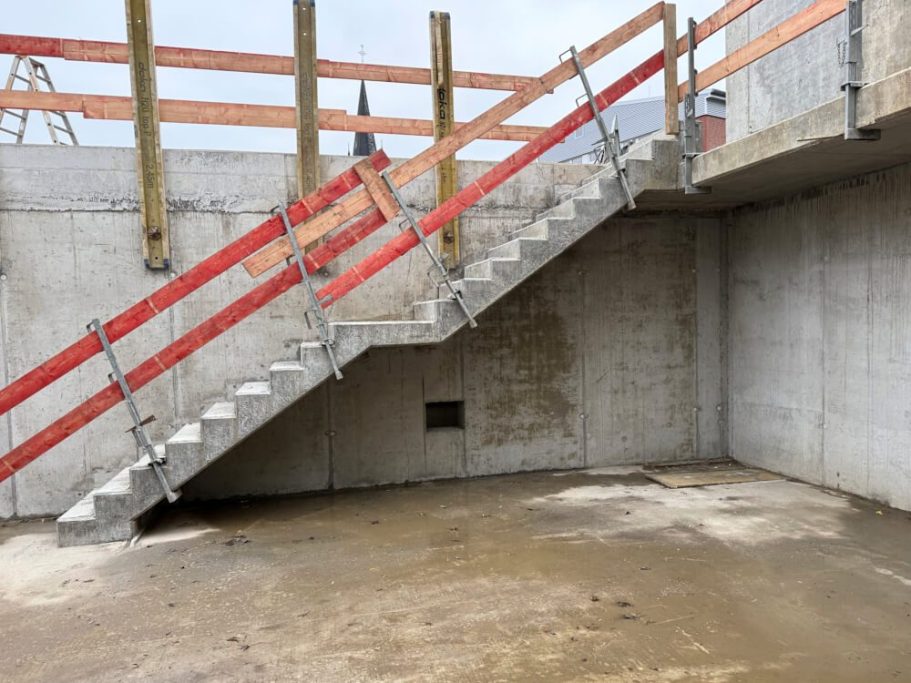 Stahltreppe mit rotem Geländer in einem unvollendeten Betonraum.