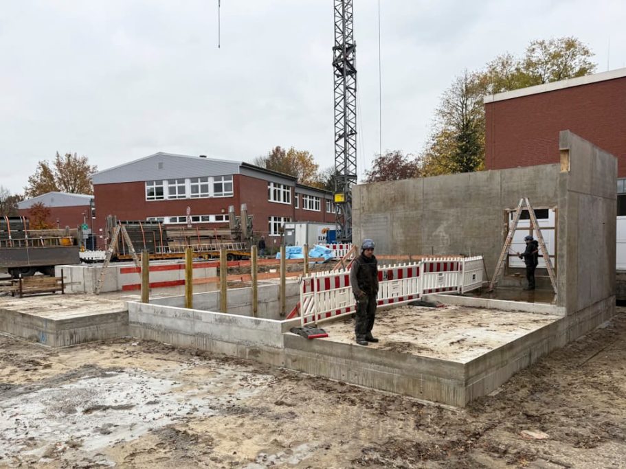 Bauplatz mit Betonfundament, Rohbau und Bauarbeitern im Hintergrund.