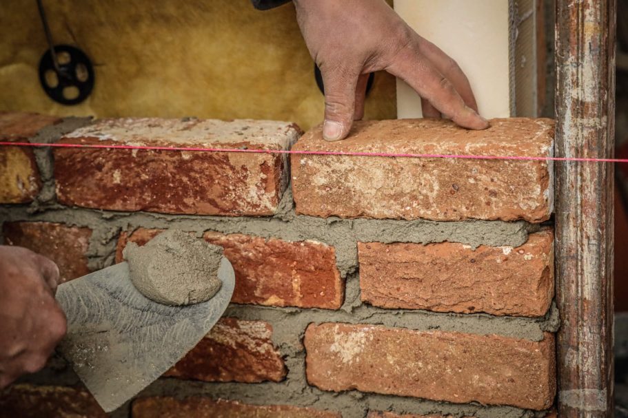 Hände legen Ziegelsteine mit Mörtel auf eine gerade Linie.